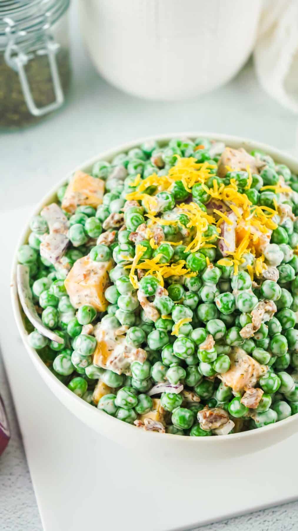 Old fashioned pea salad in a white bowl topped with shredded cheese.