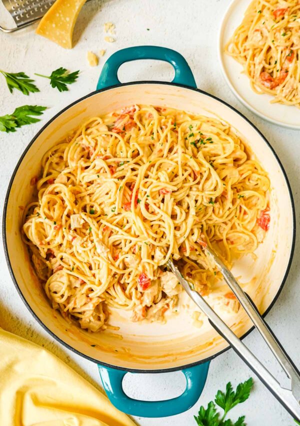 Chicken spaghetti with velveeta and rotel in a large pan with tongs.