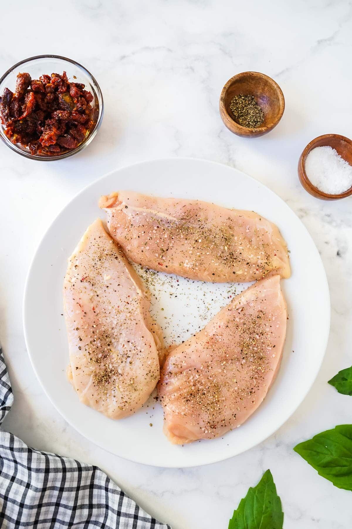 Raw chicken breasts seasoned with salt and pepper on a plate.