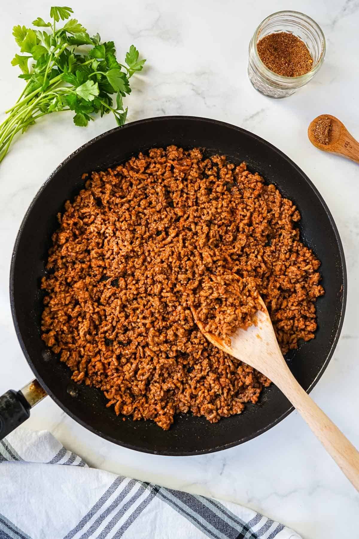 Homemade taco meat cooked in a skillet with a wooden spoon.