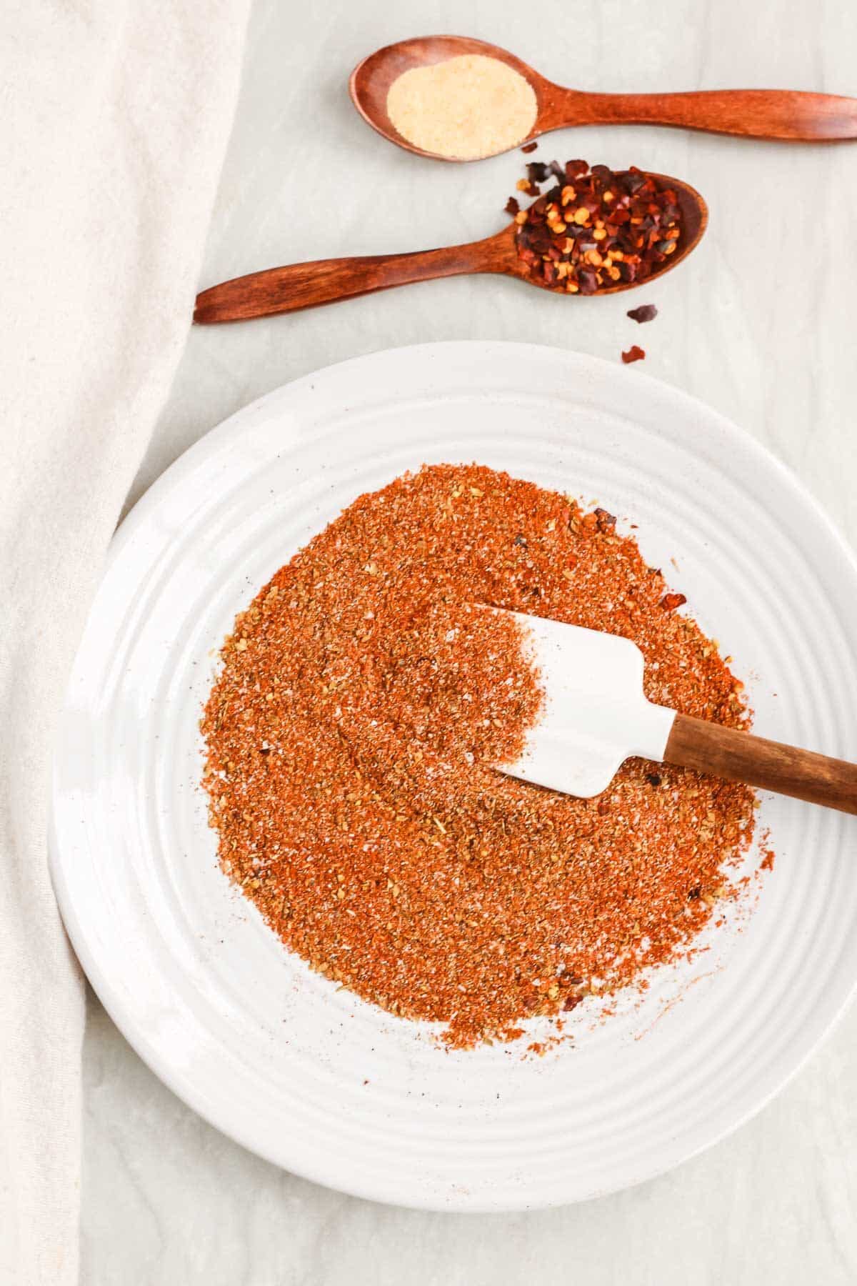 Spices for homemade low sodium taco seasoning on a plate being mixed with a white spatula.