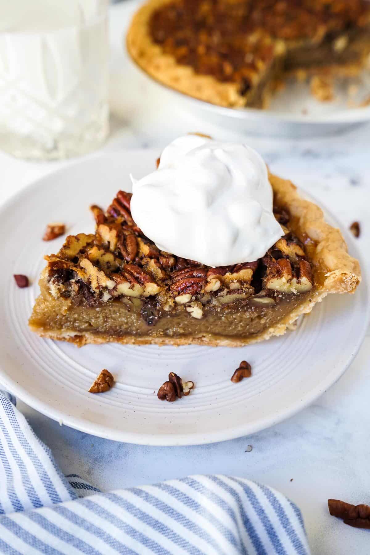 Pecan pie with whipped cream on a white plate.