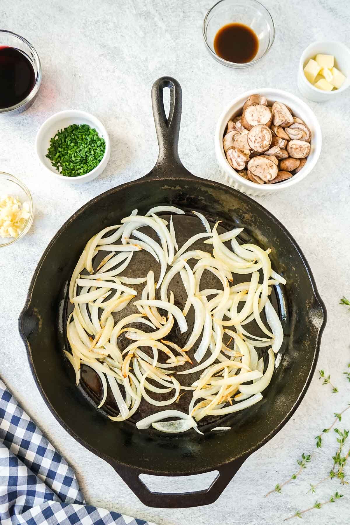Sliced onions cooking in a cast iron skillet.