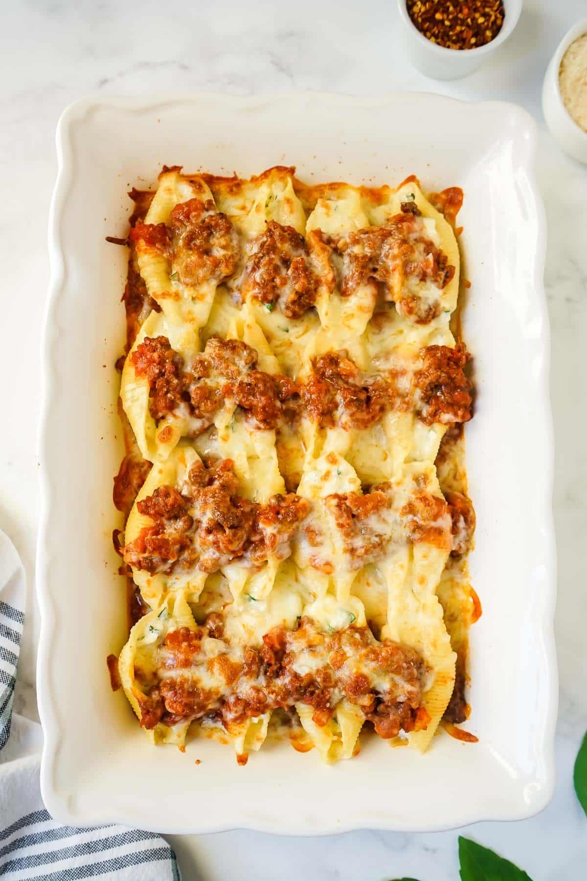 Cheesy stuffed shells with beef right out of the oven in a white casserole dish.