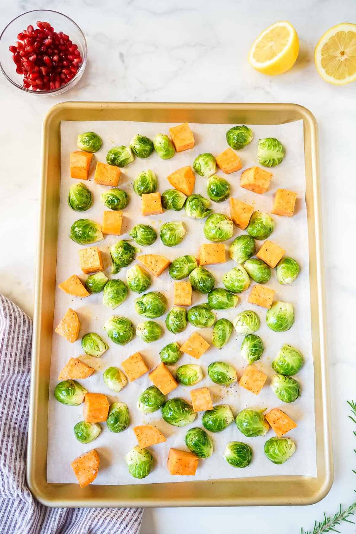 Uncooked brussels sprouts and sweet potatoes on a sheet pan.