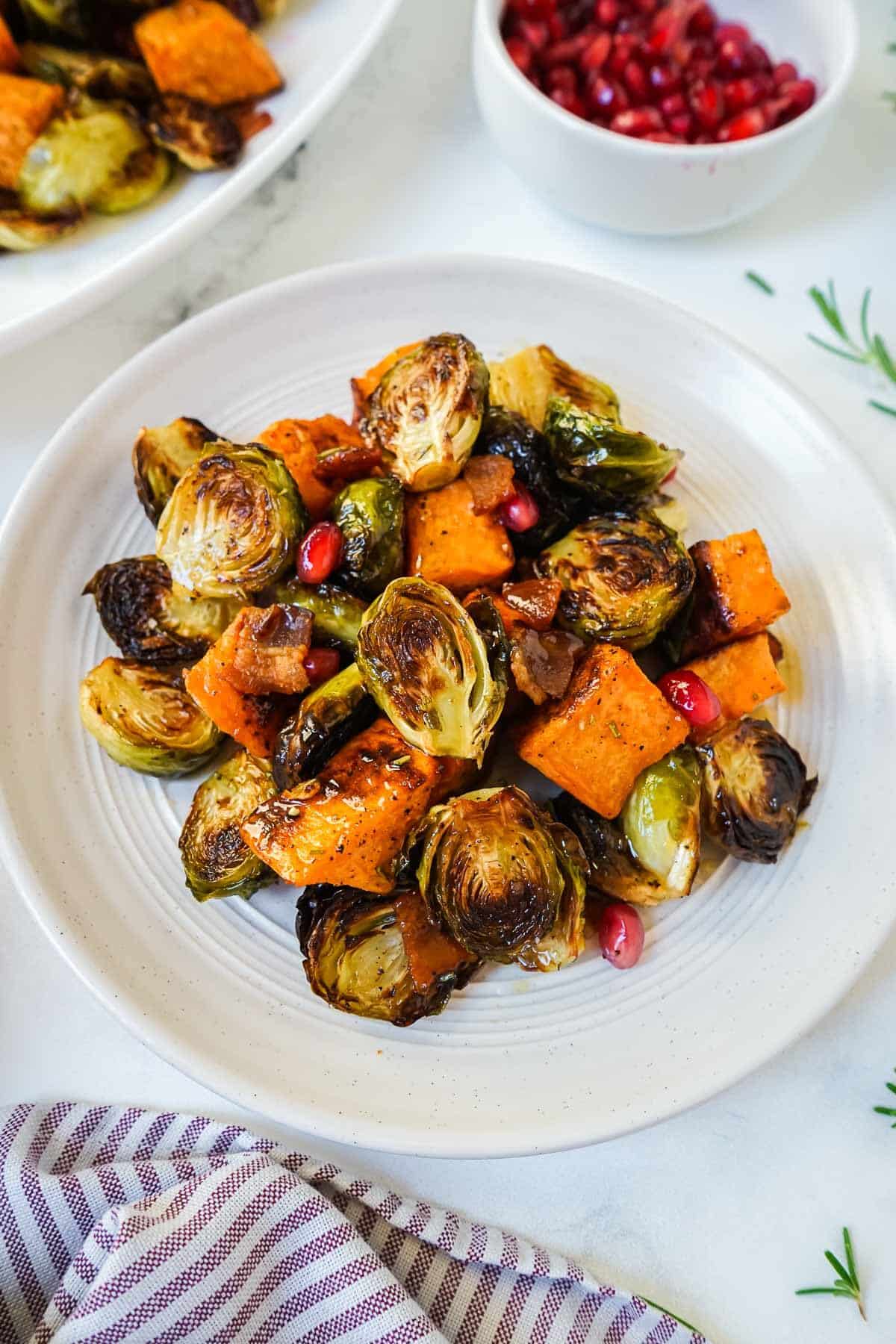 Roasted brussels sprouts and sweet potatoes on a small white plate.