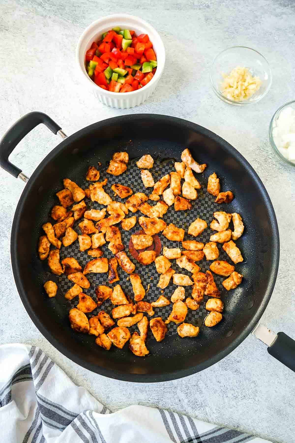 Chicken pieces being cooked in a large black pan.