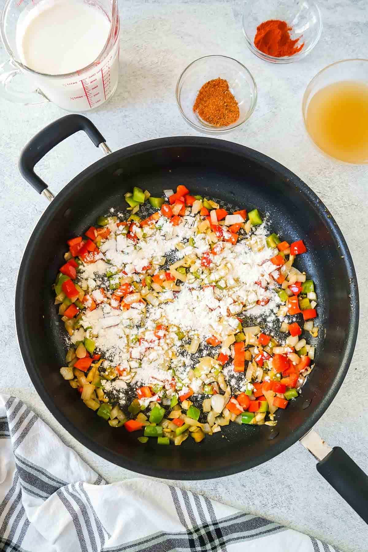 Bell peppers and onions in a large pan with flour sprinkled over the top.