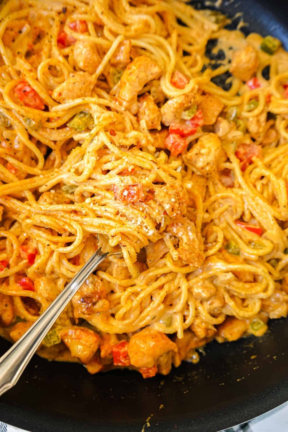 Close up shot of creamy cajun spaghetti with chicken on a fork.