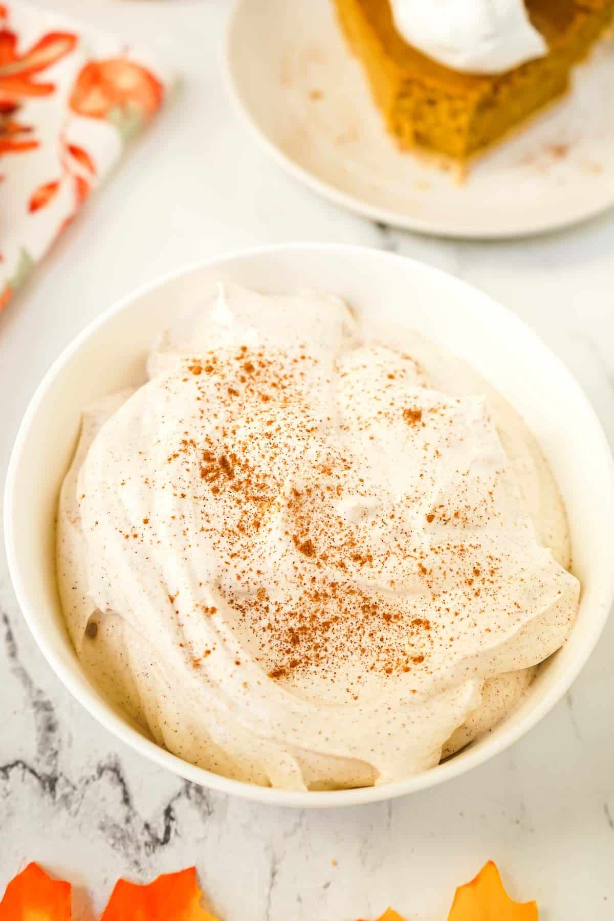 Cinnamon whipped cream in white bowl with cinnamon sprinkled on top.