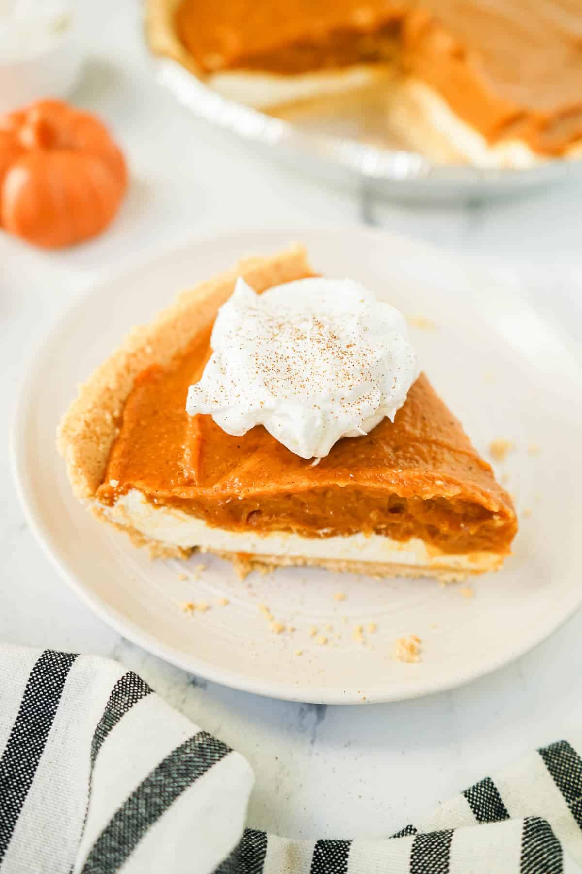 Double Layer Pumpkin pie with whipped cream on a white plate.