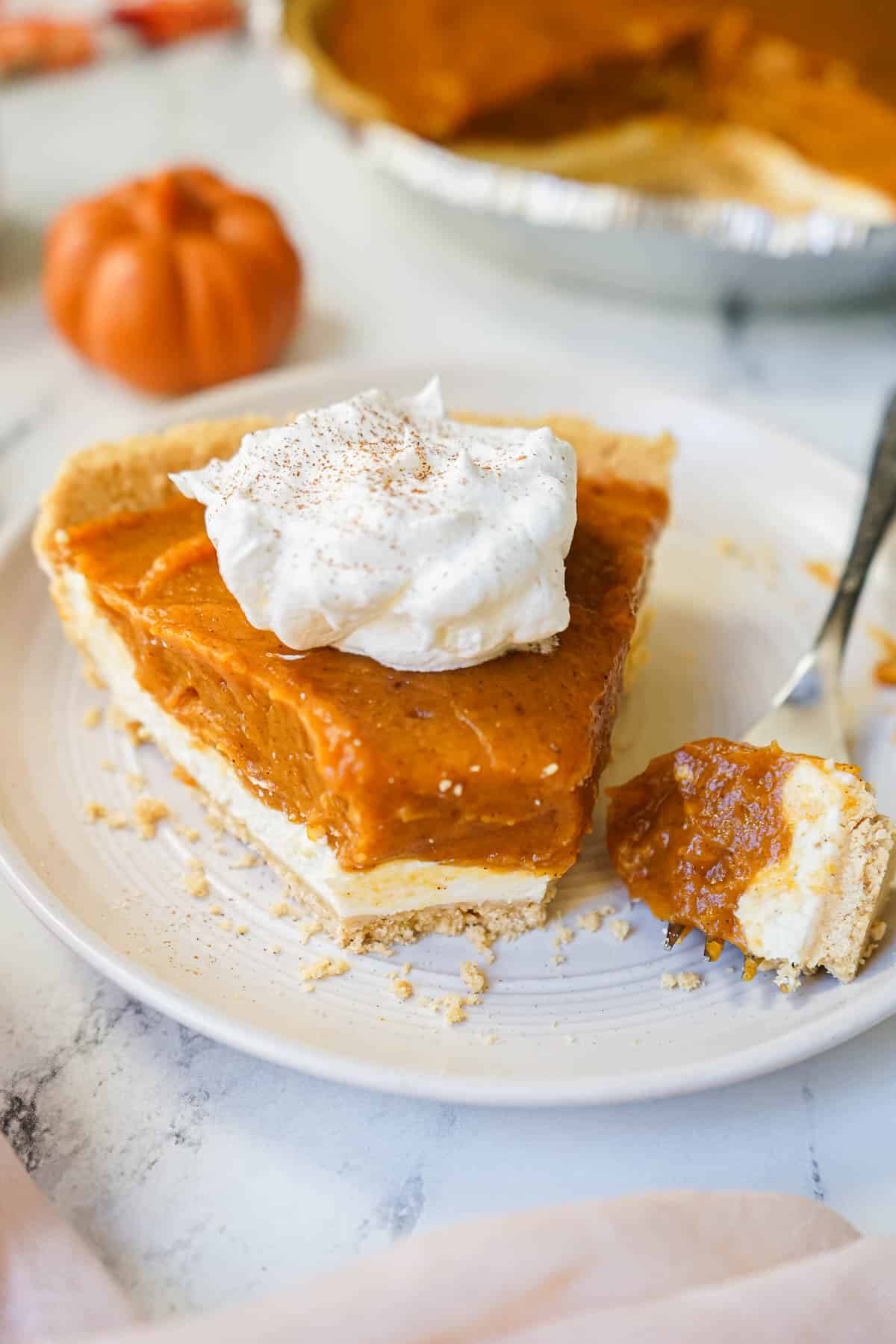 A piece of double layer pumpkin pie on a plate with a fork.
