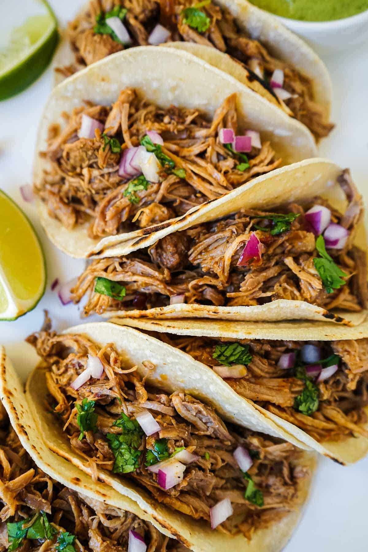 Pork carnitas tacos on a plate with lime and red onion.