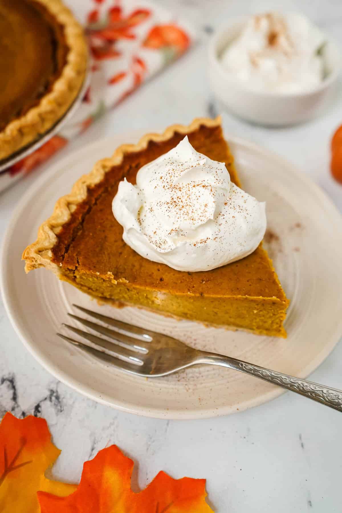 A slice of pumpkin pie with whipped cream on a plate with a fork.