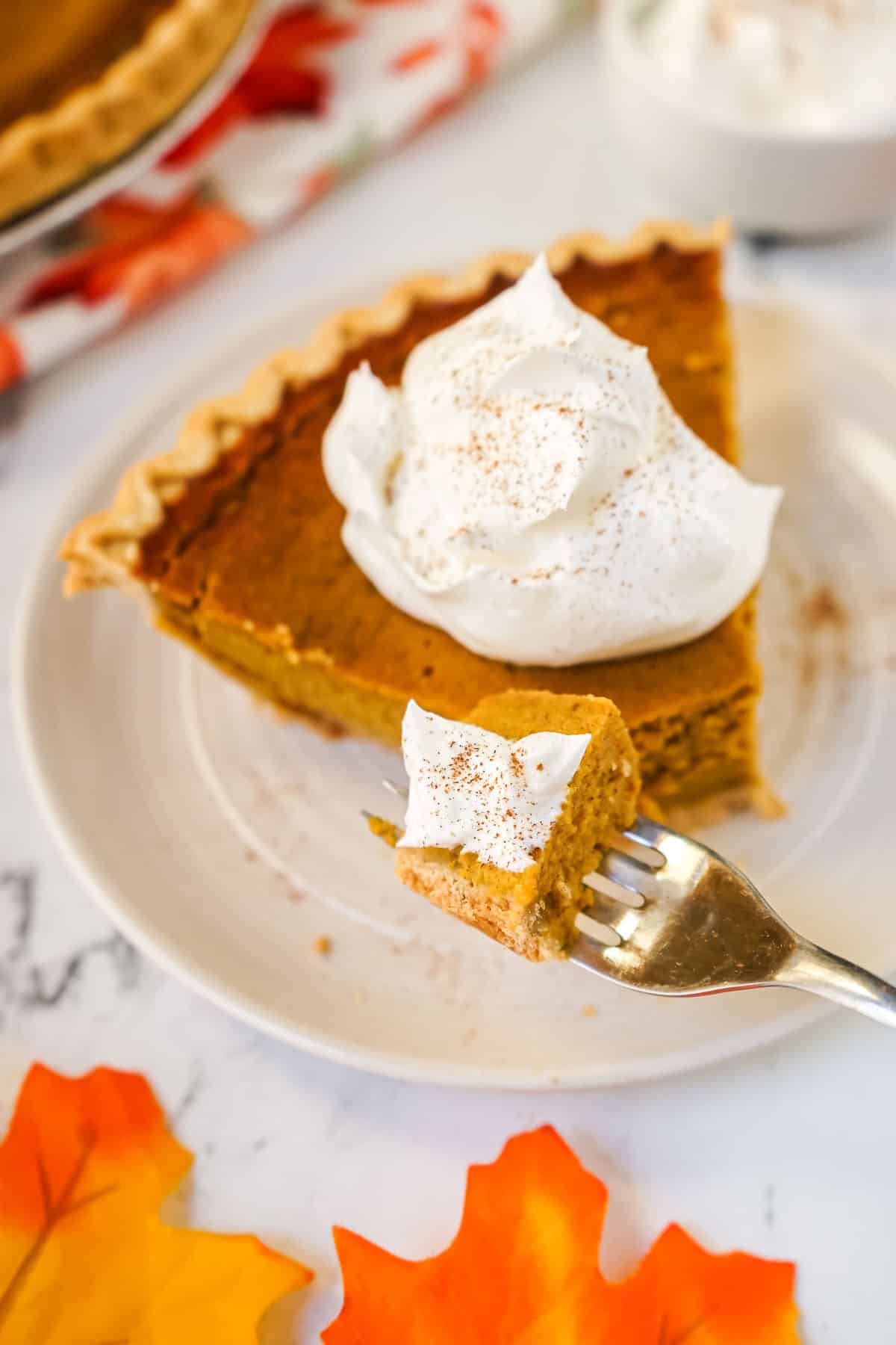 A piece of pumpkin pie without evaporated milk on a fork with whipped cream.