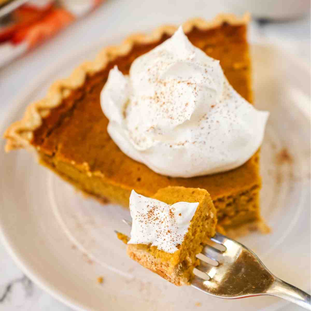 A slice of pumpkin pie made without evaporated milk on a plate with a fork and whipped cream.