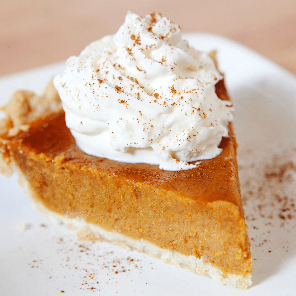 One piece of pumpkin pie with whipped cream on a white plate.
