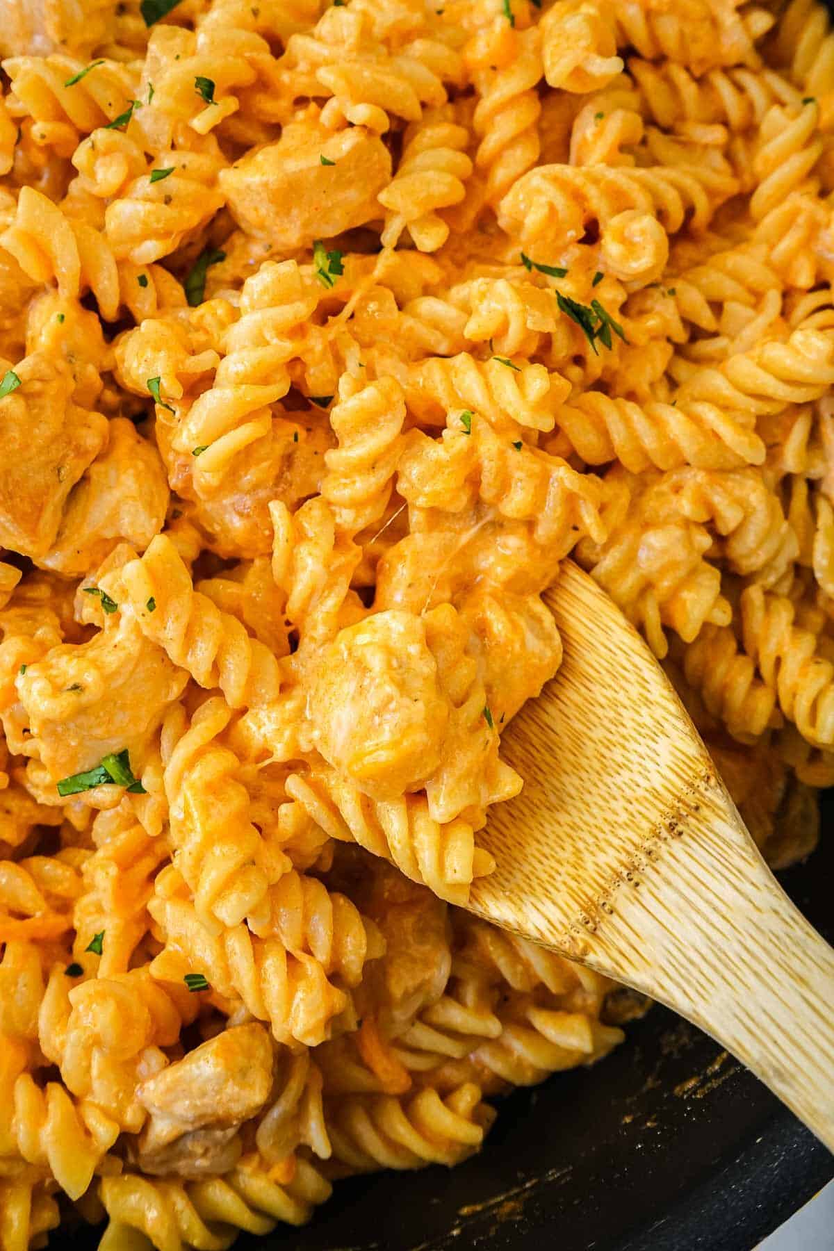 Buffalo chicken pasta in a skillet with a close up of the pasta on a wooden spoon.