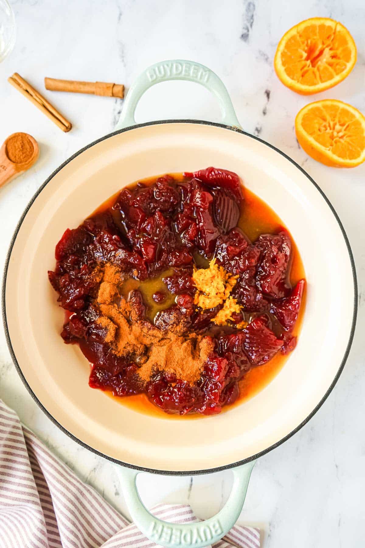 Canned cranberry sauce in a arge saucepan with cinnamon, orange zest and other ingredients. 