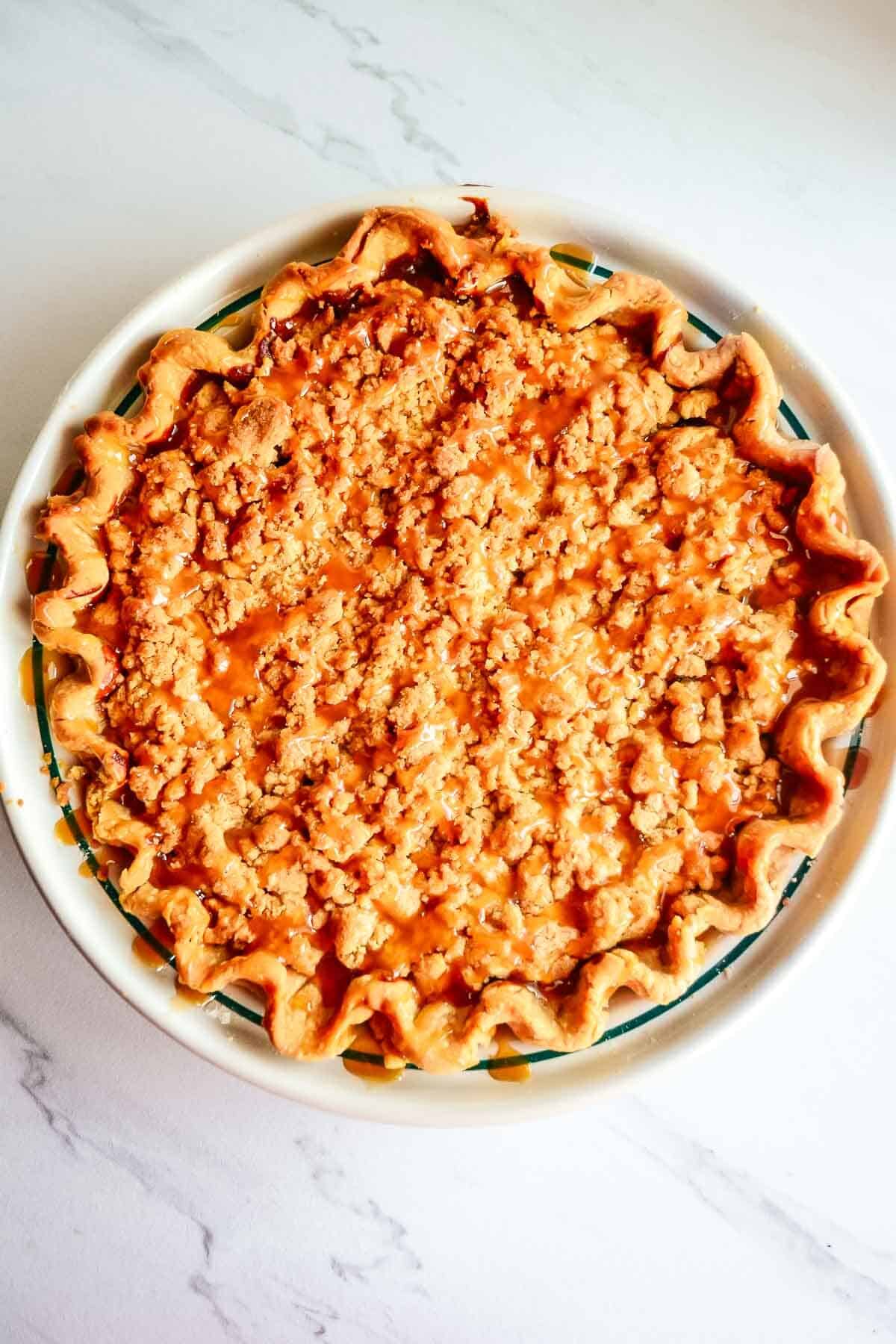 Pie shell filled with caramel apples with the crumb topping after being baked and drizzled with caramel sauce.