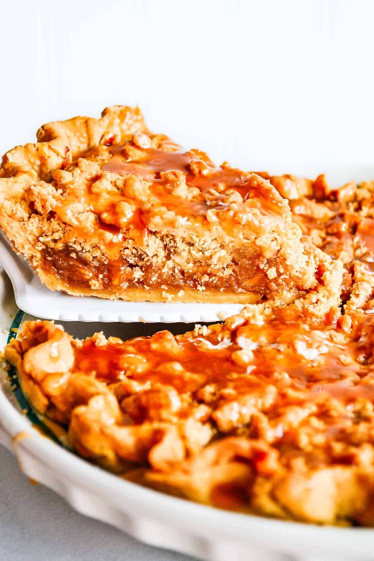 A large piece of caramel apple pie with crumb topping on a pie server.