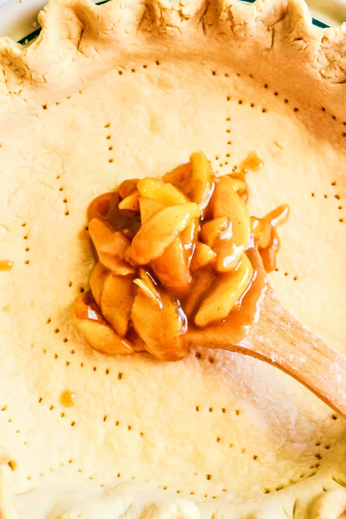 Caramel apple pie filling being spooned into a pie crust.