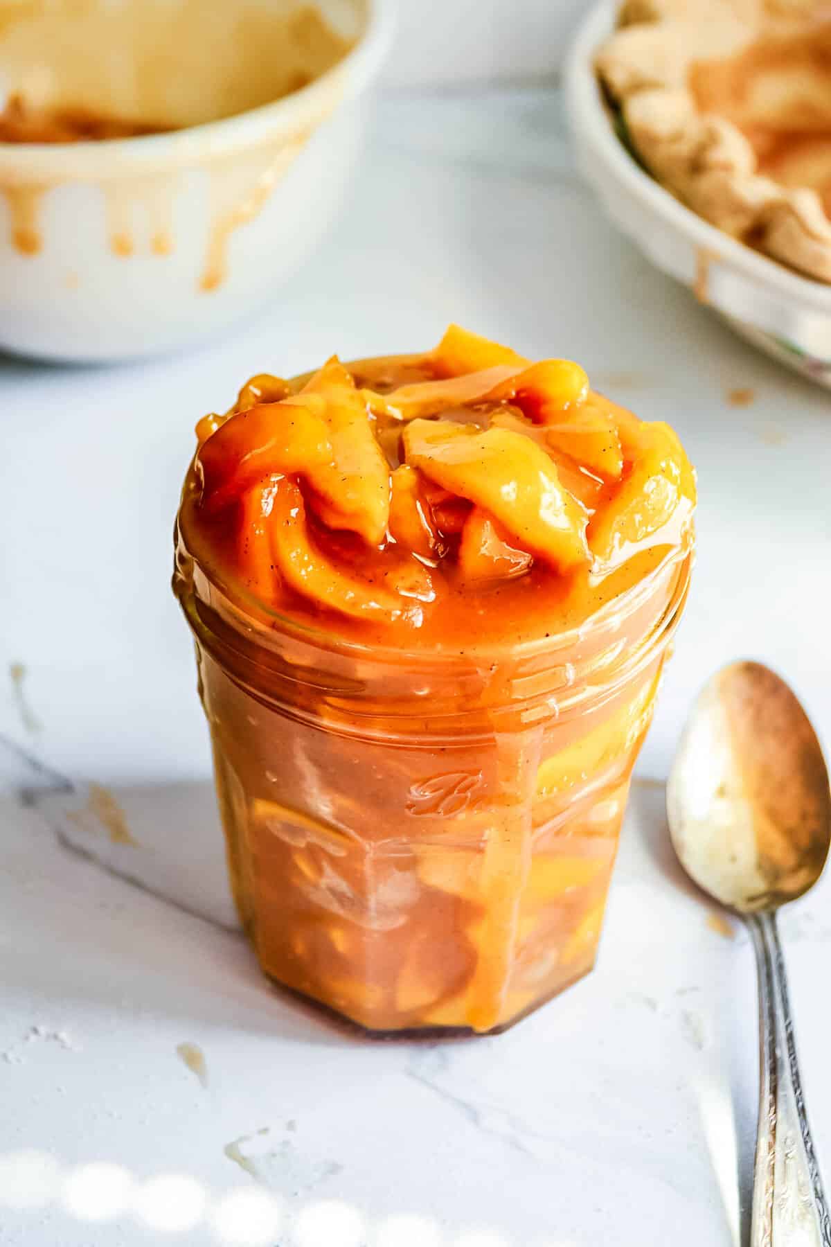 Caramel apple pie filling in a glass jar with a spoon.