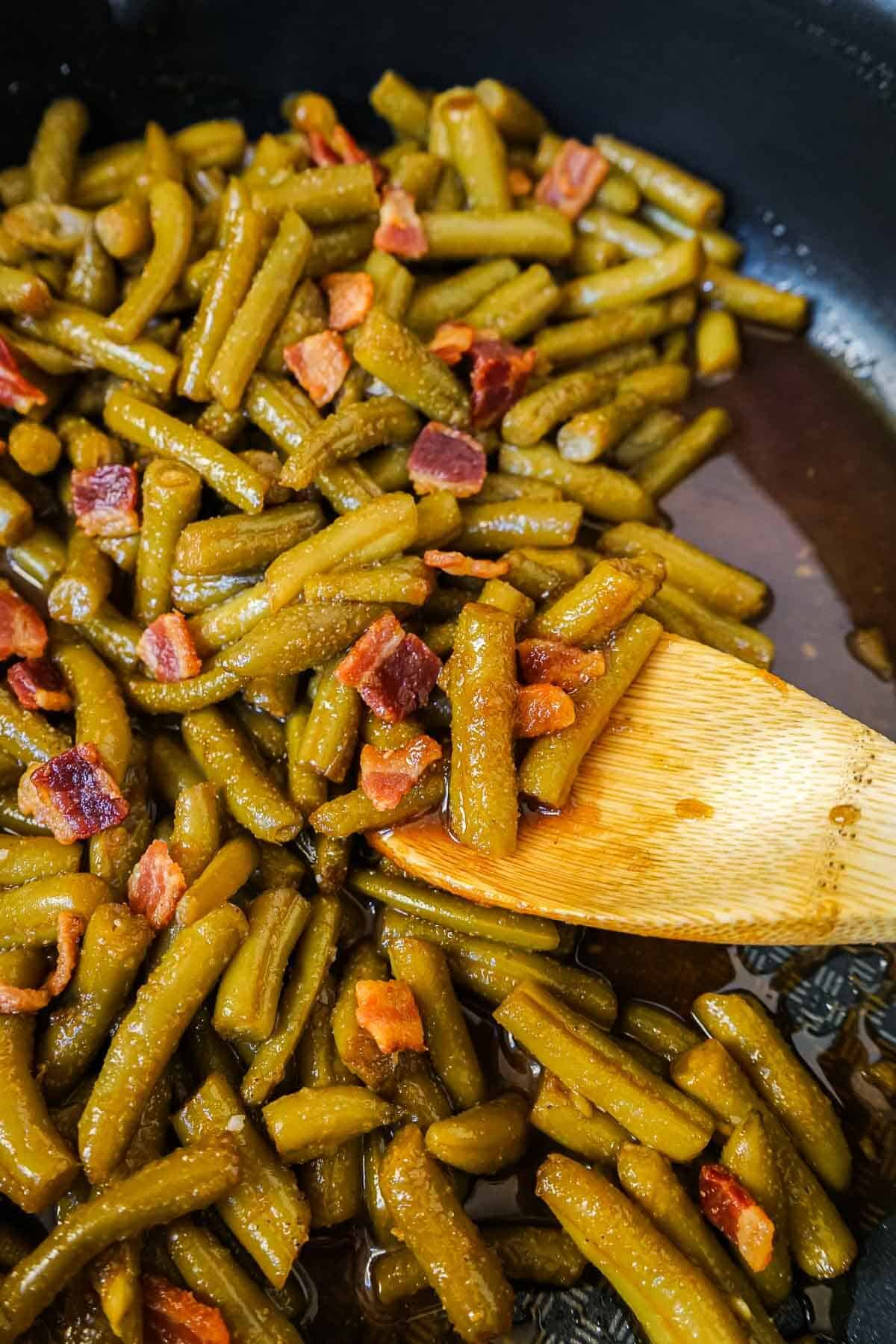 Close up of crack green beans recipe in a skillet with a wooden spoon.