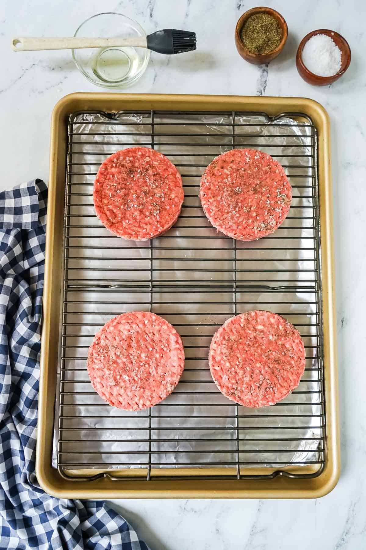 Frozen hamburgers on a baking sheet sprinkled with salt and pepper.