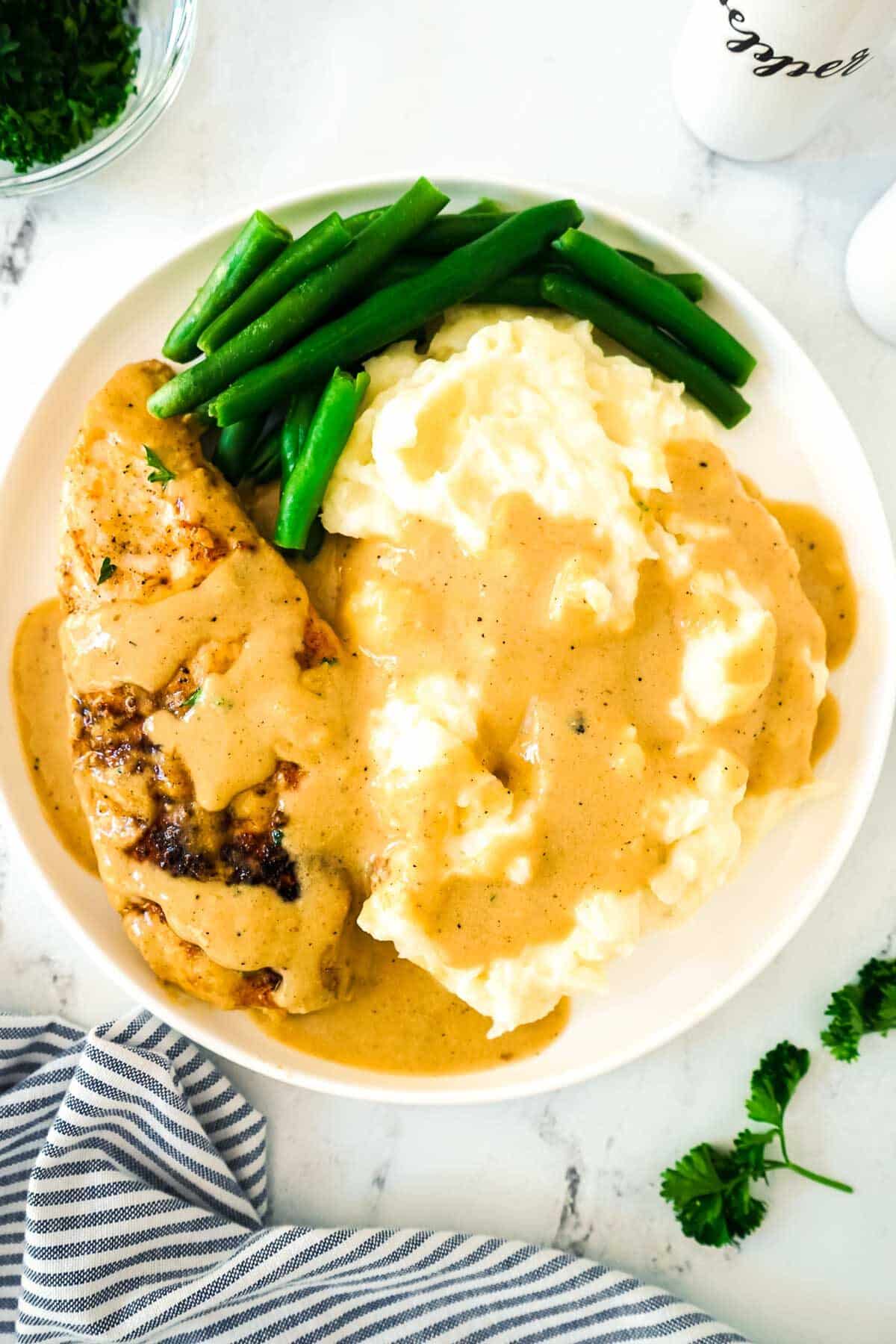 Creamy chicken with mashed potatoes on a white plate with green beans.