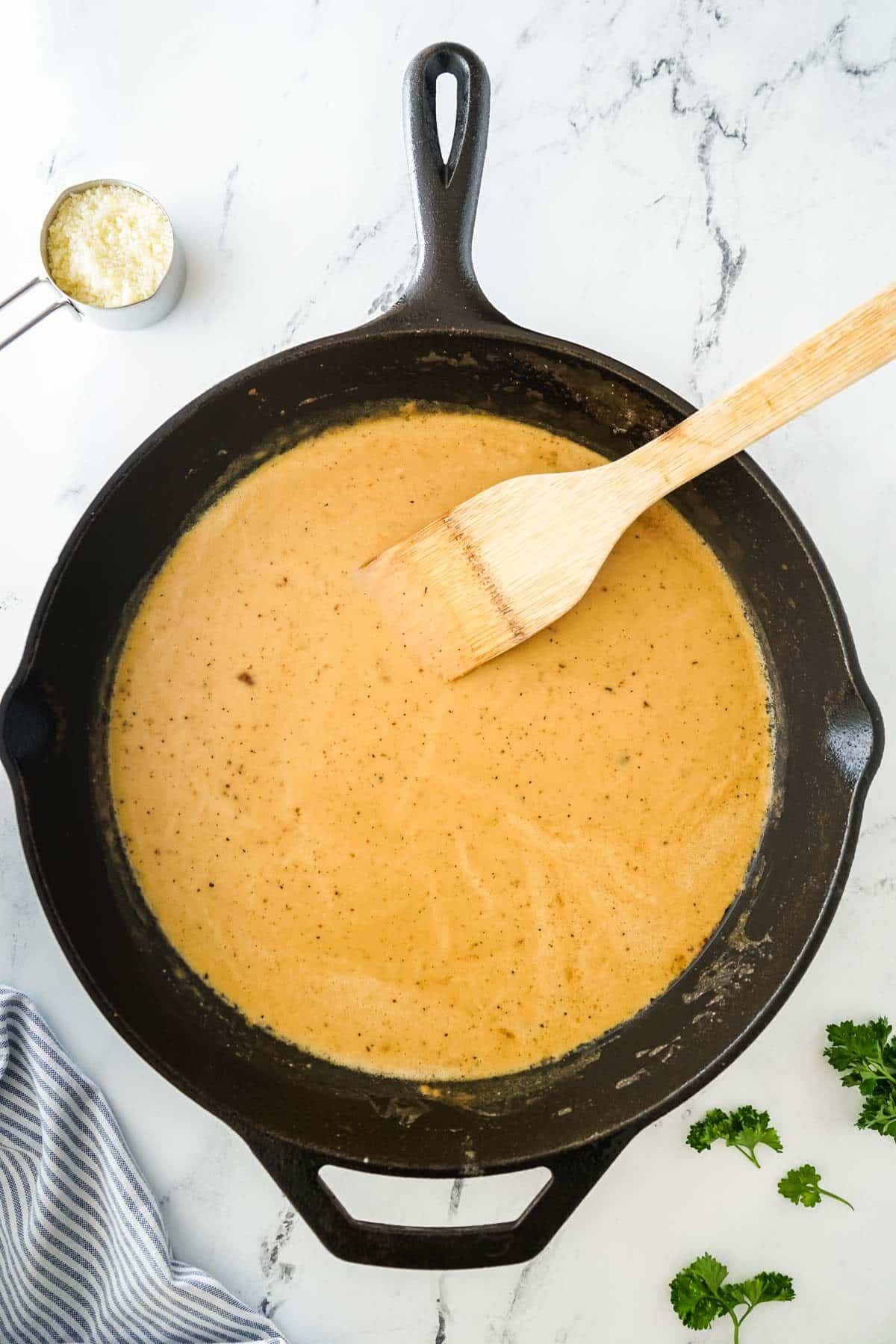 Sauce for the creamy chicken with mashed potatoes being cooked in a cast iron pan.