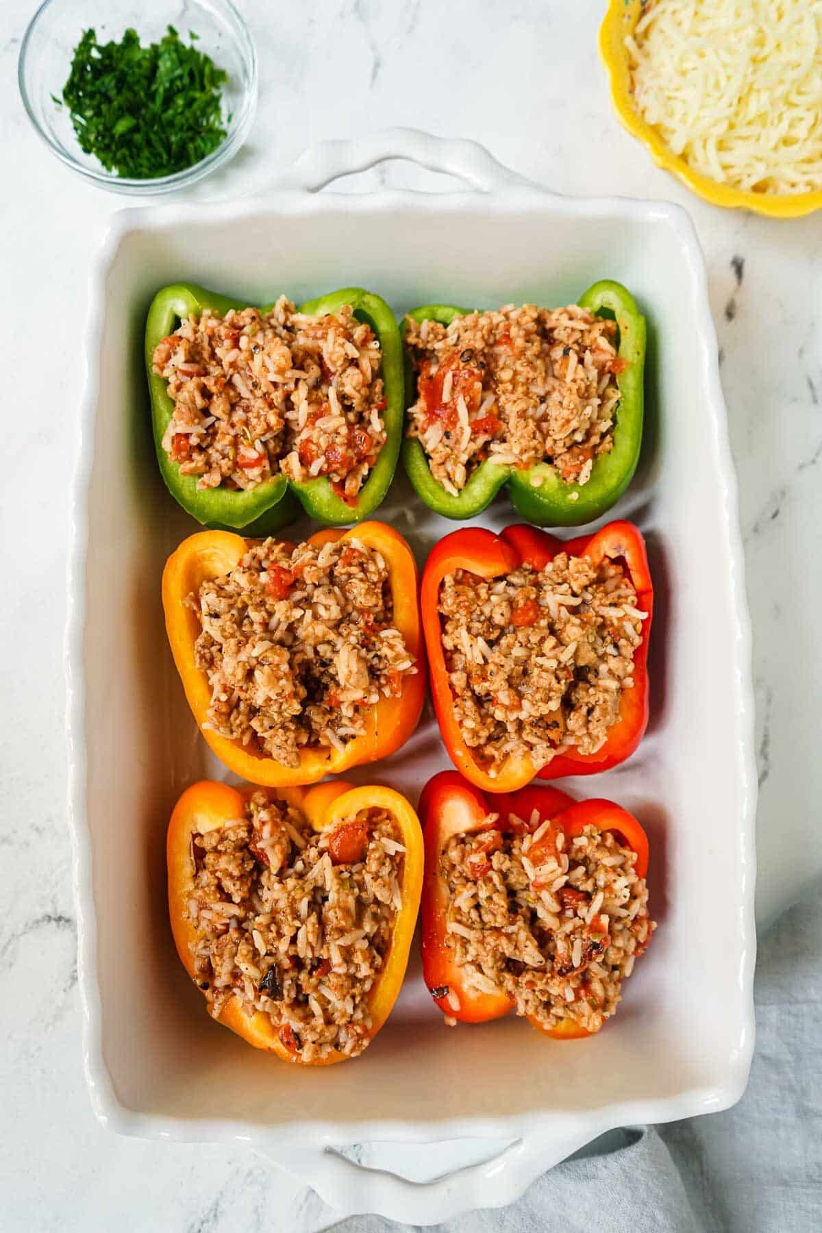 Bell peppers that are filled with stuffing in a white casserole dish before being cooked.