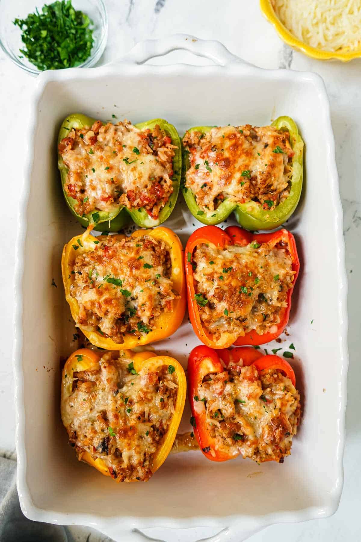 Bell peppers that are filled with stuffing in a white casserole dish after being cooked.