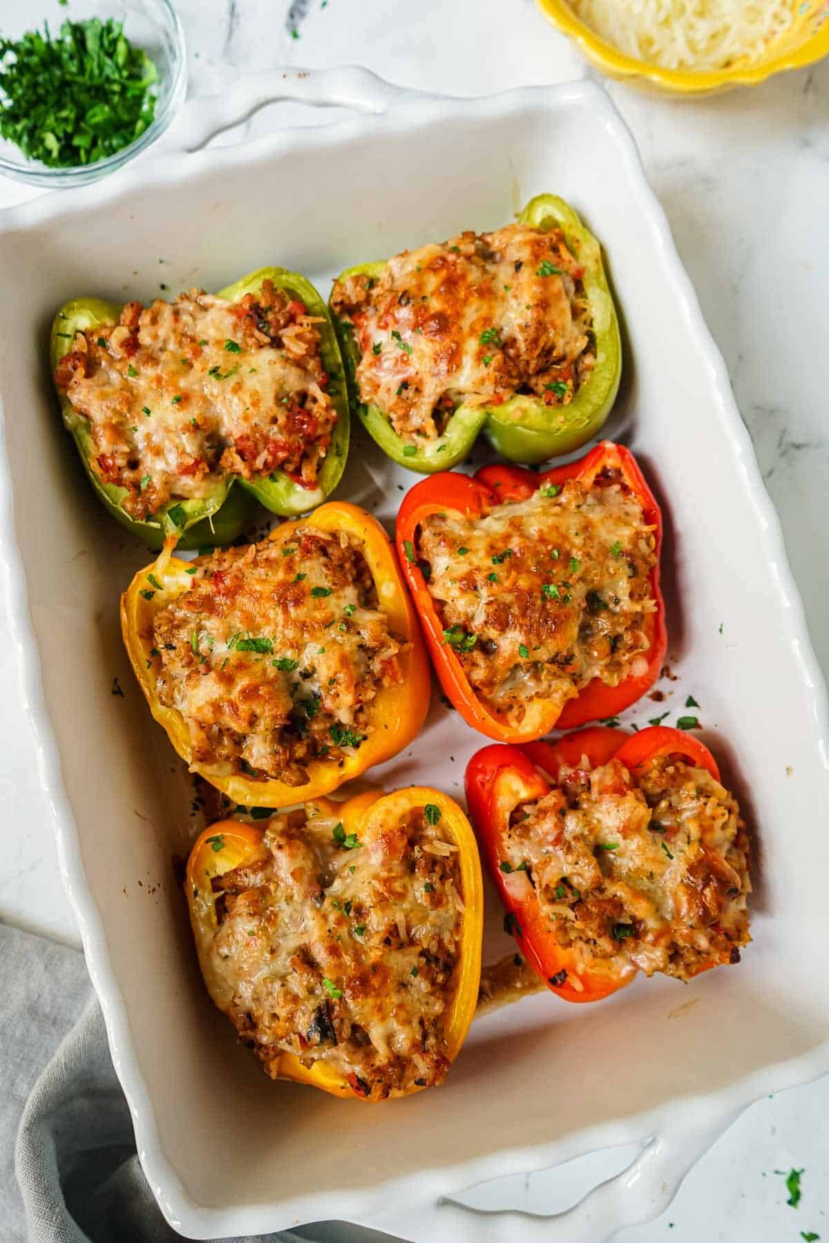 Six Italian Sausage Stuffed Peppers topped with cheese in a white baking dish.