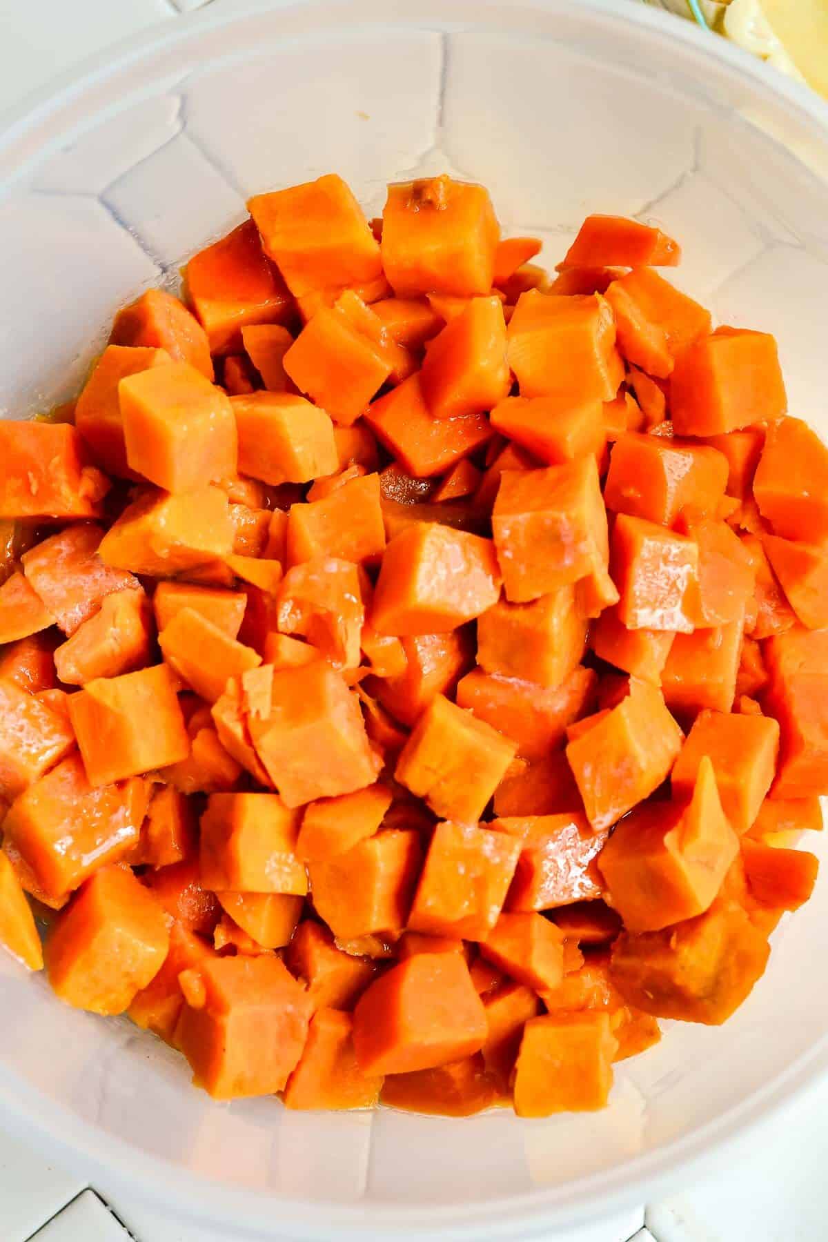 Cubed sweet potatoes, cooked, in a large glass bowl.