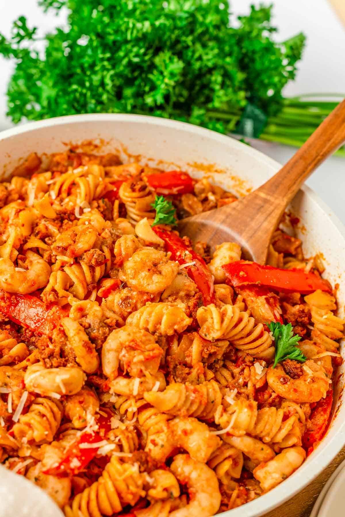 A white bowl of creamy Cajun shrimp and sausage pasta with a wooden spoon.