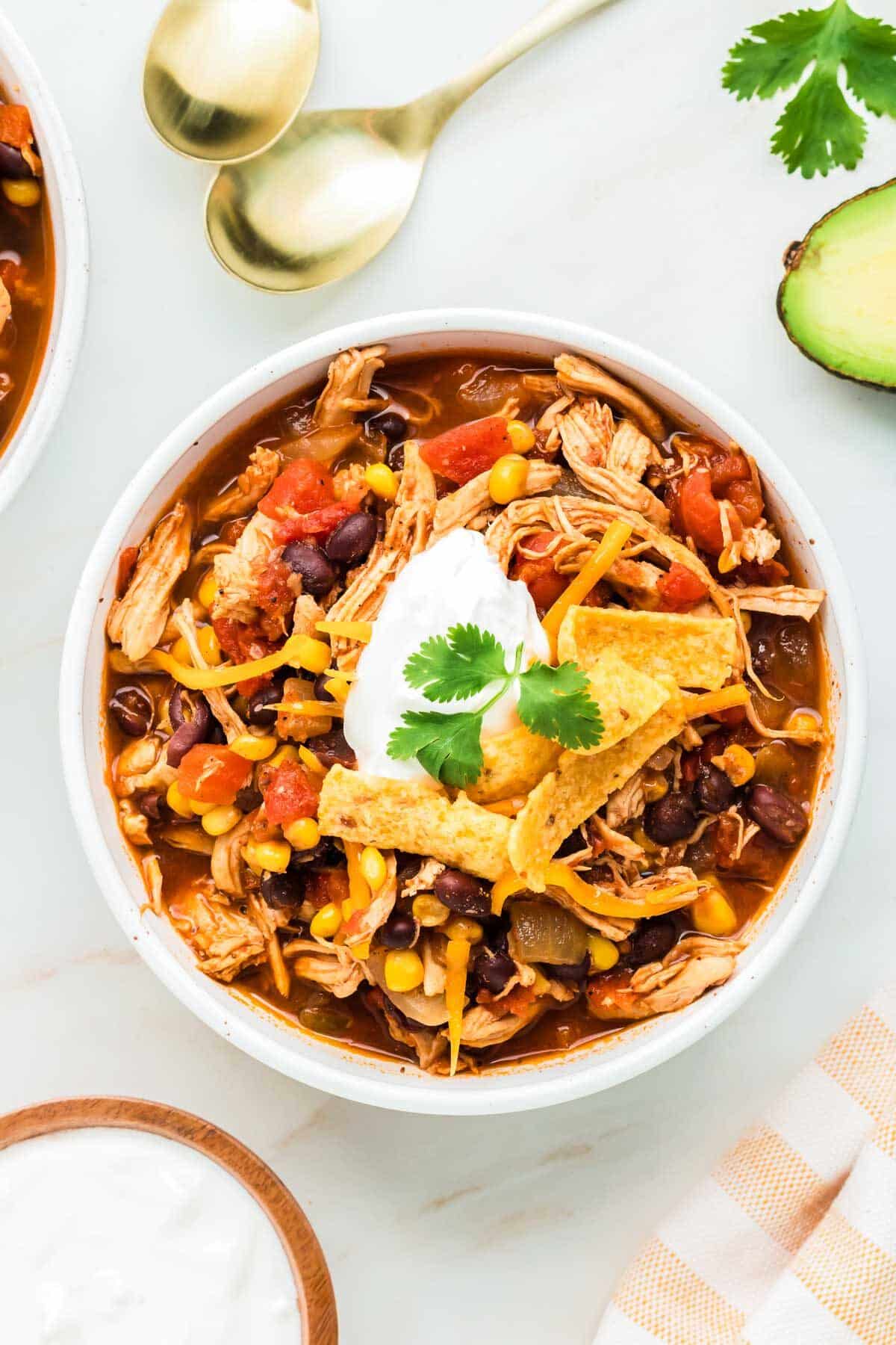 red chicken chili in a white bowl with Fritos and sour cream.