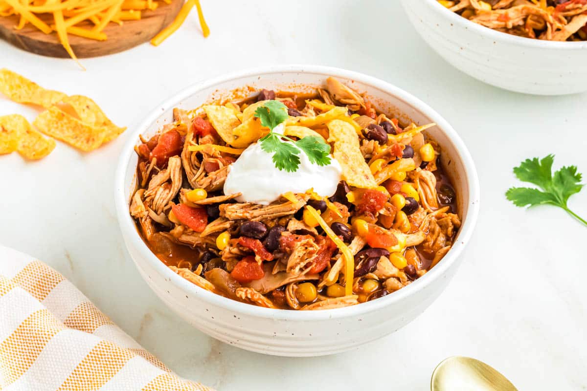 Red chicken chili made with shredded chicken in a bowl, with lots of chili toppings.