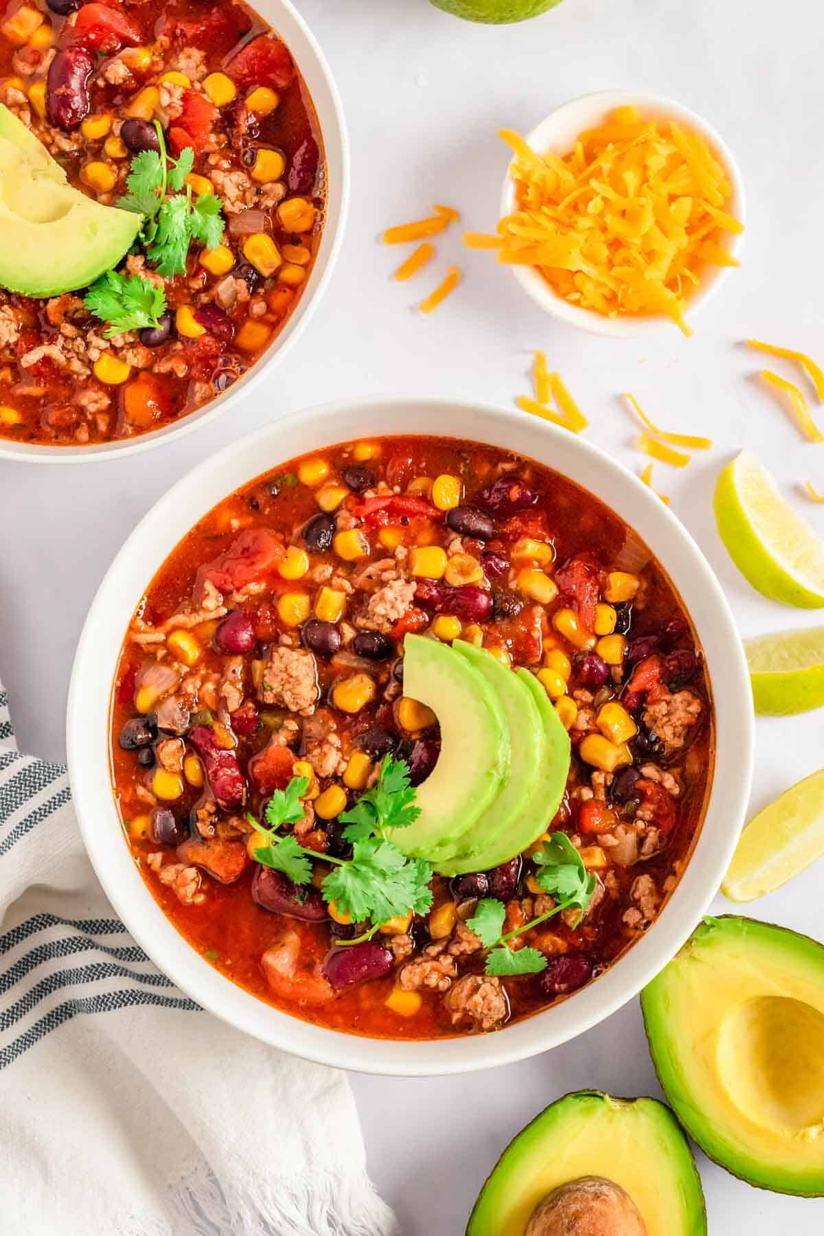 Easy Crockpot or Stovetop Taco Soup with Ranch Dressing in a white bowl with avocado and cilantro.