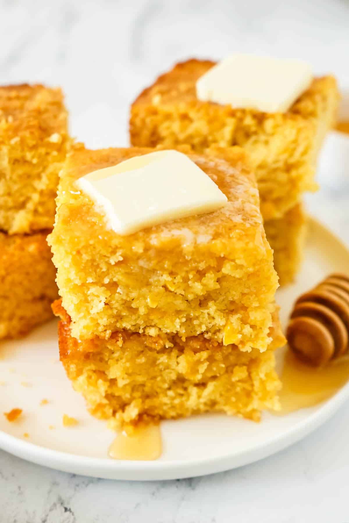 A plate of Sweet Jiffy Cornbread on a white plate with honey and butter.