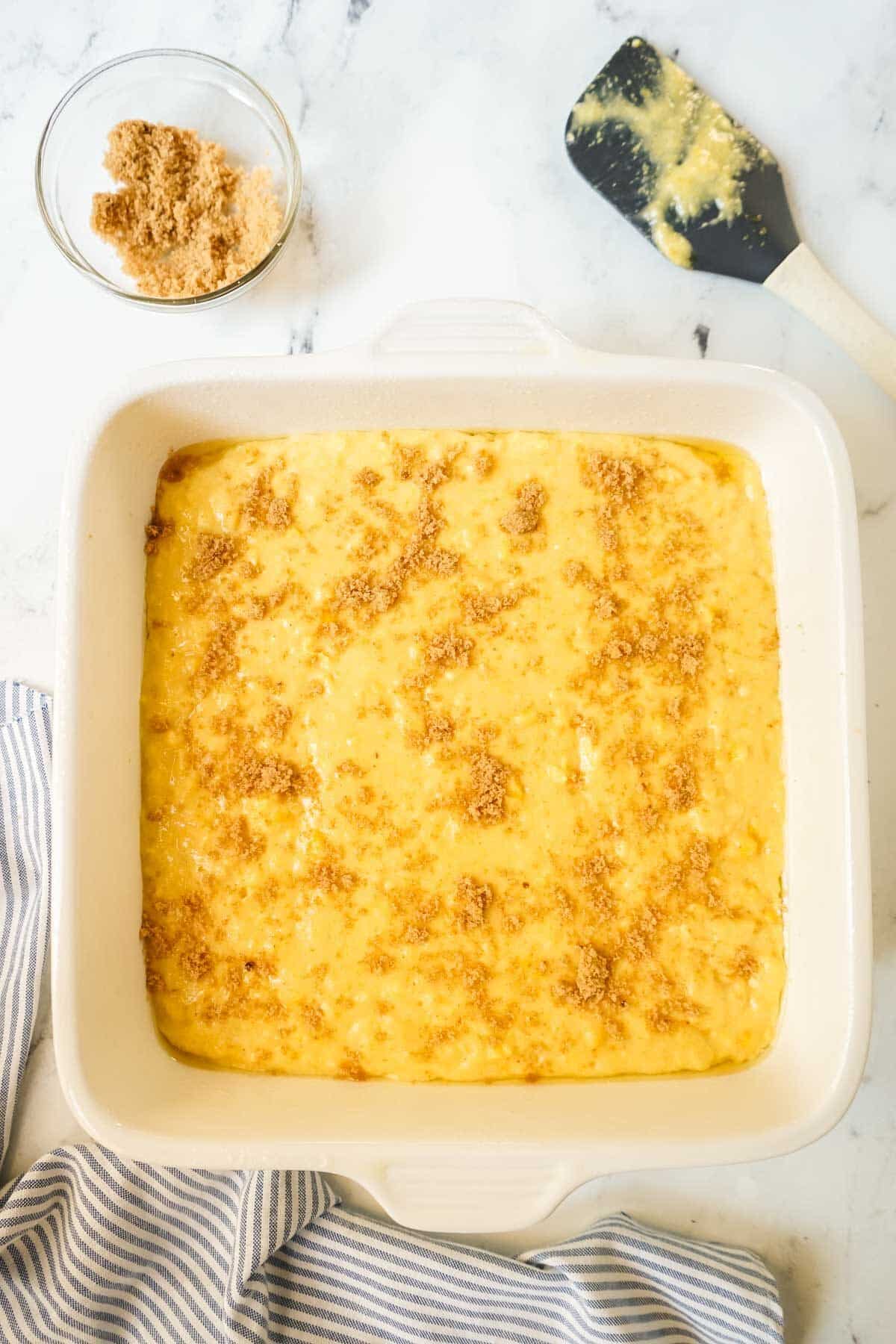 Cornbread batter poured into a white baking dish and sprinkled with brown sugar.