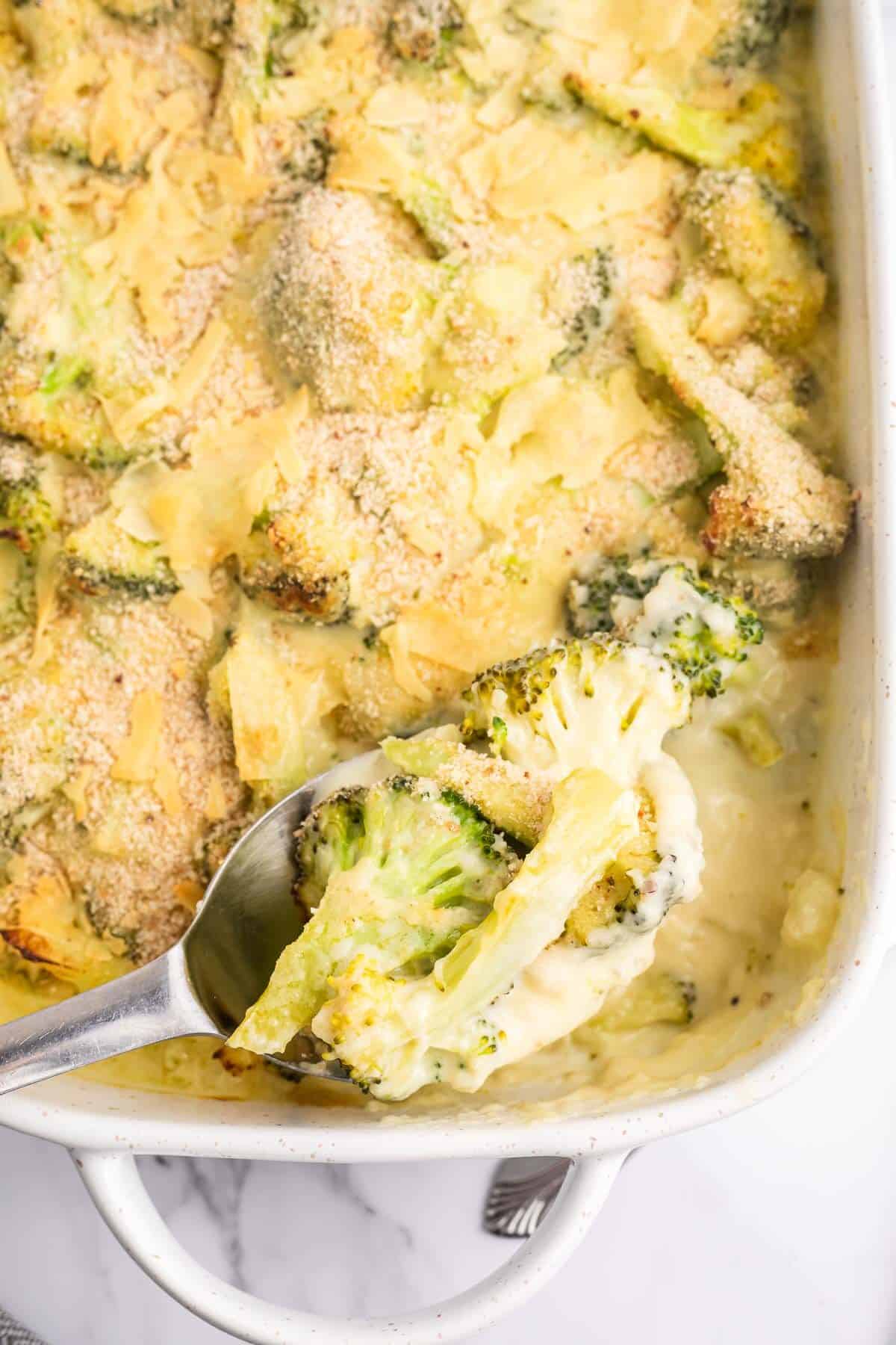 Cheesy Broccoli Au Gratin in a pan being scooped out with a spoon.