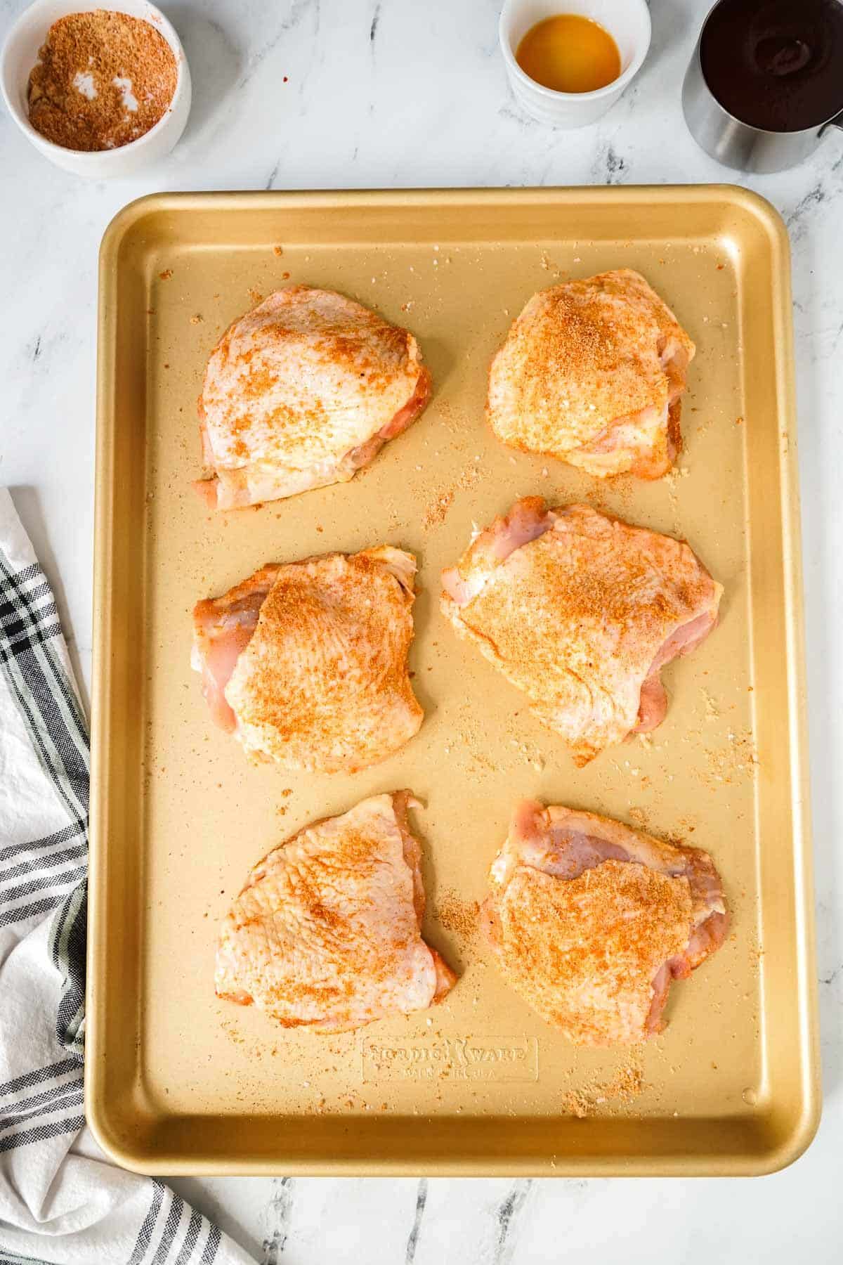 Chicken thighs on a baking sheet coated with a spice rub.