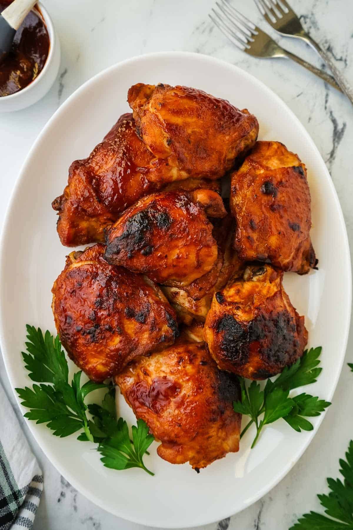 Slow cooker BBQ chicken thighs on a white platter.
