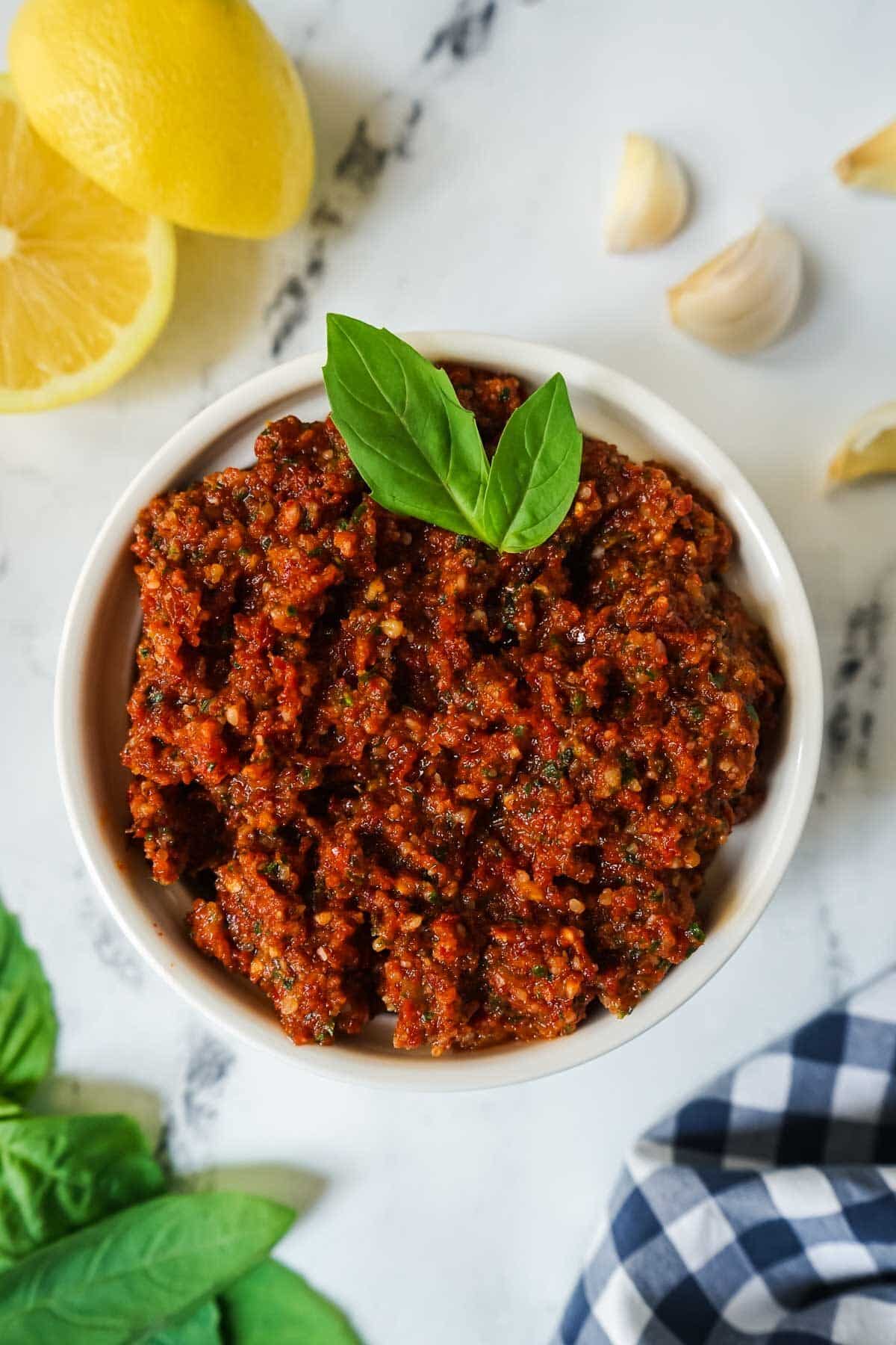 Sun dried tomato pesto in a white bowl garnished with two basil leaves.
