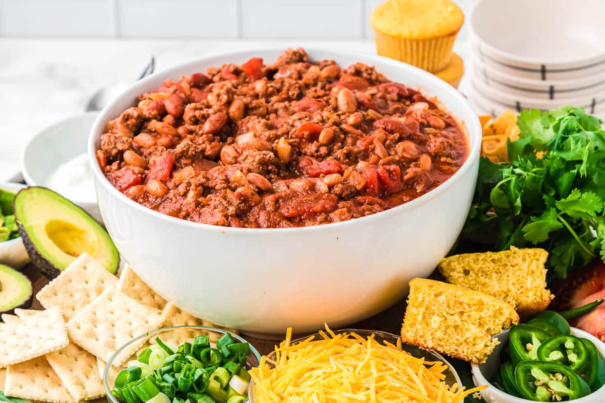 A big bowl of three bean chili in a white bowl with all the fixings.