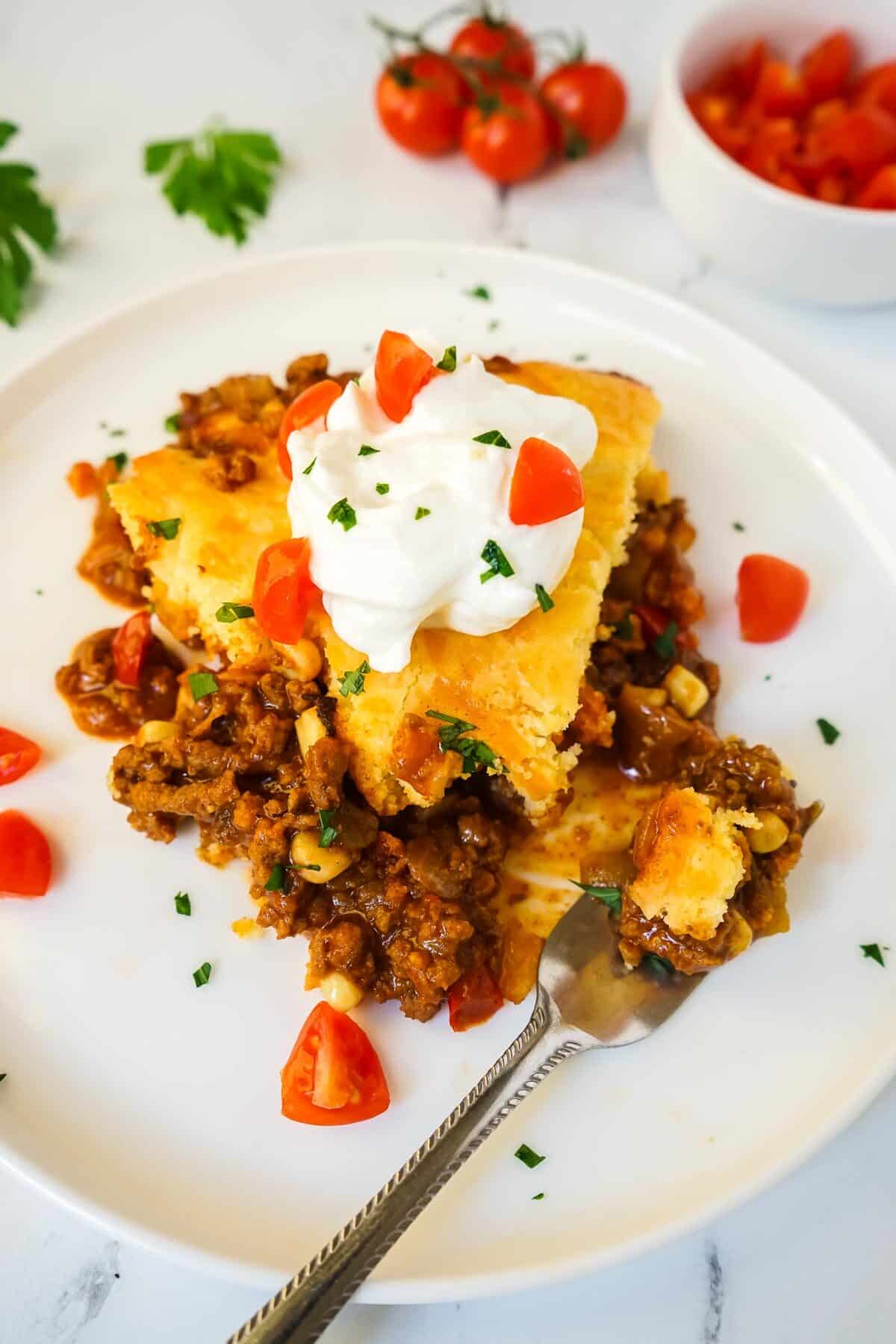 A slice of Jiffy Tamale Pie on a white plate topped with sour cream.