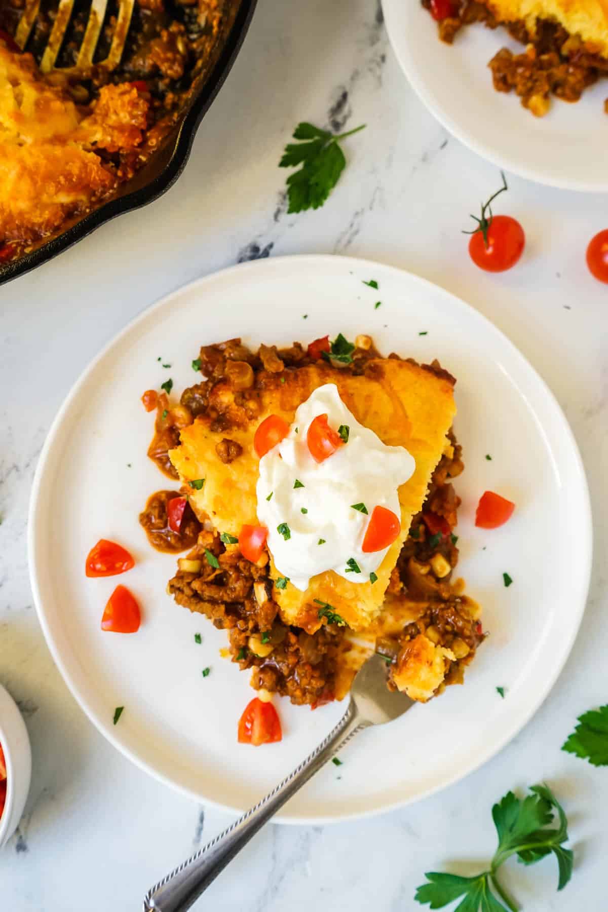 A slice of Jiffy Tamale Pie on a white plate topped with sour cream.
