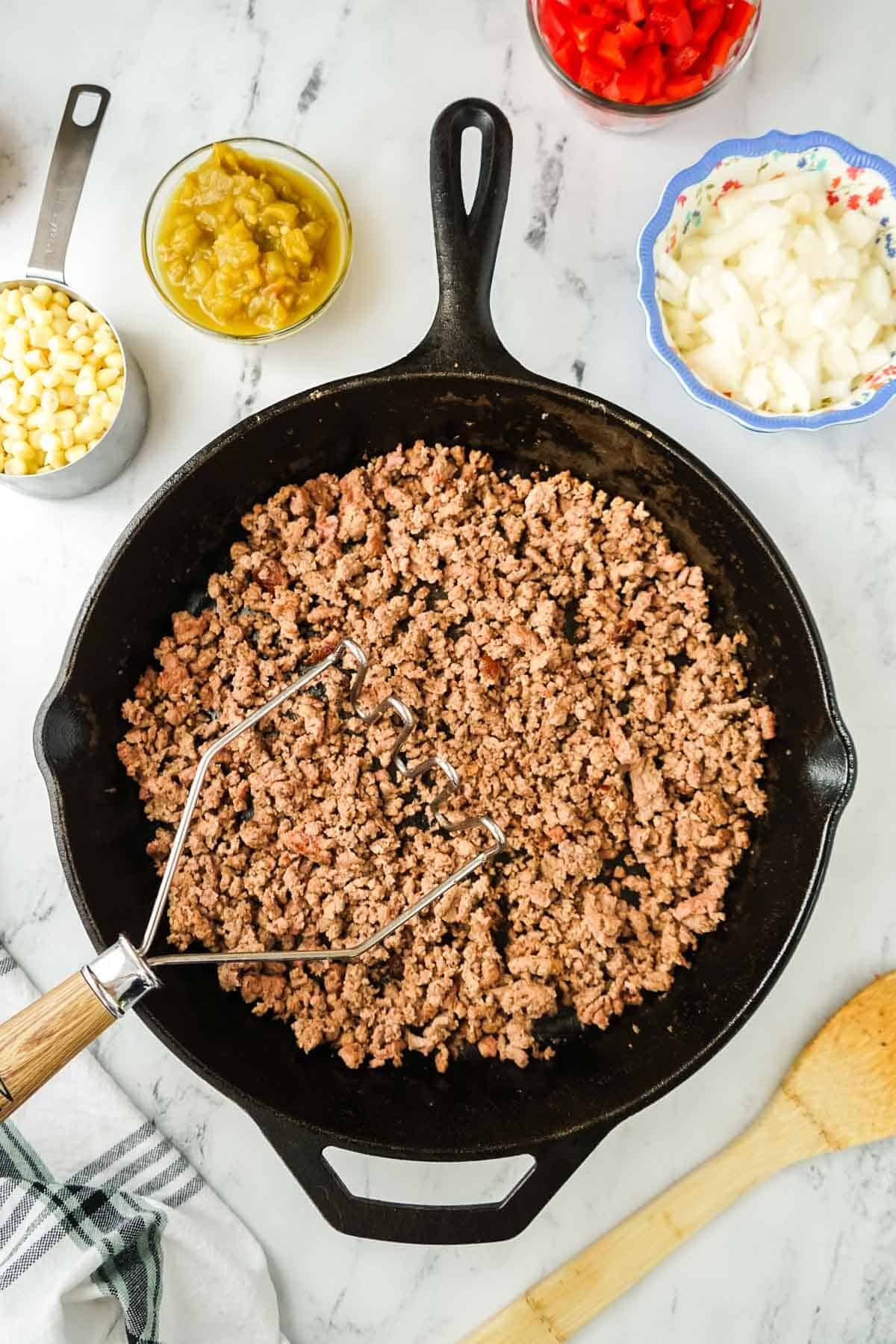 Ground beef browning in a cast iron skillet.