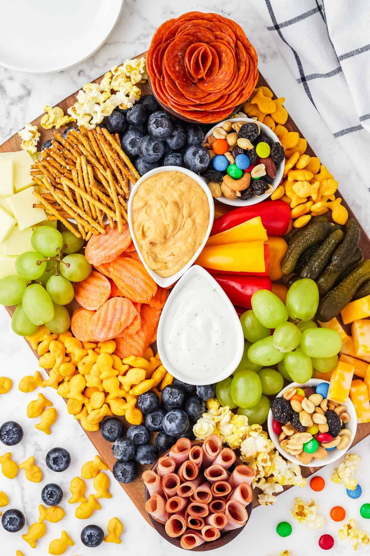 Kid's Charcuterie Board with fruit, crackers and dips on a large wooden board.